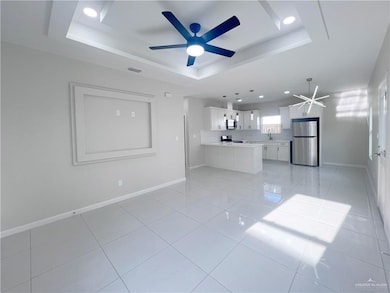 Unfurnished living room featuring a raised ceiling, ceiling fan, light tile patterned flooring, recessed lighting, and a chandelier