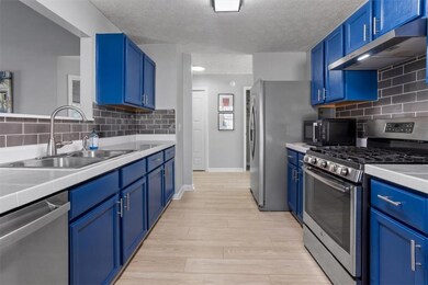 Kitchen featuring tile counters, appliances with stainless steel finishes, backsplash, blue cabinetry, and a textured ceiling