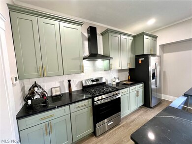 Kitchen featuring green cabinetry, appliances with stainless steel finishes, light hardwood / wood-style flooring, tasteful backsplash, and wall chimney exhaust hood