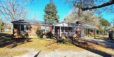 Ranch-style home with brick siding, aphalt driveway, a porch, a chimney, and a carport