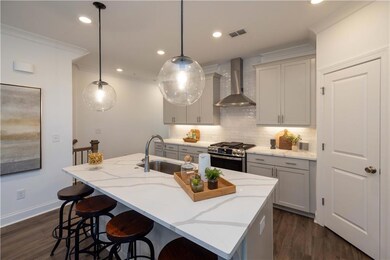 Kitchen with stainless steel gas stove, wall chimney exhaust hood, a sink, decorative backsplash, and a breakfast bar area
