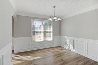 Spare room featuring arched walkways, crown molding, a chandelier, a textured ceiling, and a wainscoted wall