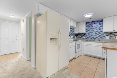 Kitchen featuring white appliances, light tile patterned floors, a sink, white cabinetry, and backsplash