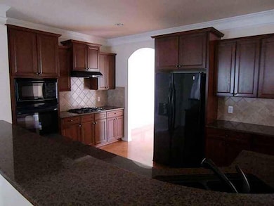 Kitchen with arched walkways, dark stone countertops, black appliances, tasteful backsplash, and crown molding