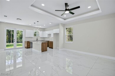 Kitchen with a raised ceiling, light marble finish floors, white cabinetry, a center island, and recessed lighting