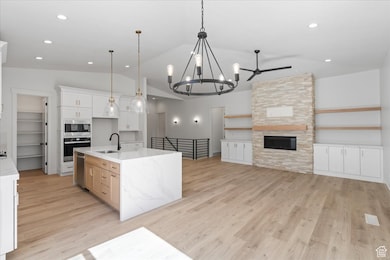Kitchen featuring a sink, stainless steel appliances, open floor plan, light wood-type flooring, and lofted ceiling