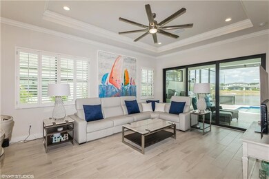 Living room featuring a raised ceiling, ceiling fan, light wood finished floors, and ornamental molding