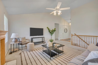 Carpeted living area with a fireplace, a ceiling fan, and high vaulted ceiling
