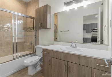 Full bath with vanity, enclosed tub / shower combo, toilet, and wood finished floors