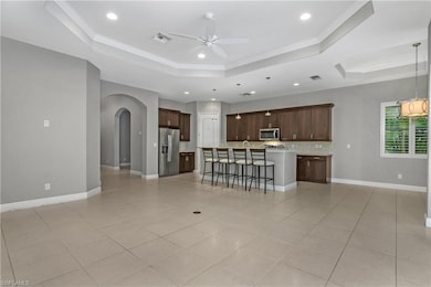 Kitchen featuring a tray ceiling, arched walkways, a breakfast bar, ornamental molding, and light tile patterned flooring