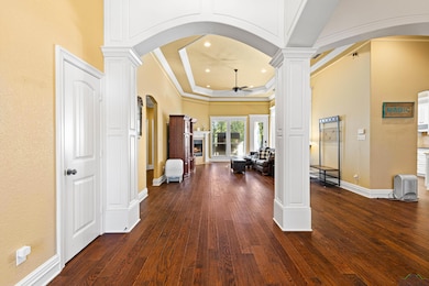 Corridor with arched walkways, decorative columns, dark wood-type flooring, a raised ceiling, and ornamental molding