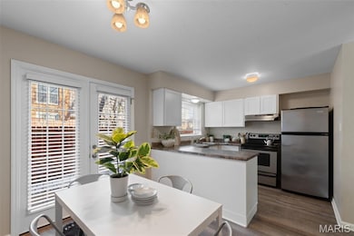 Kitchen with appliances with stainless steel finishes, dark countertops, decorative backsplash, dark wood-type flooring, and white cabinets