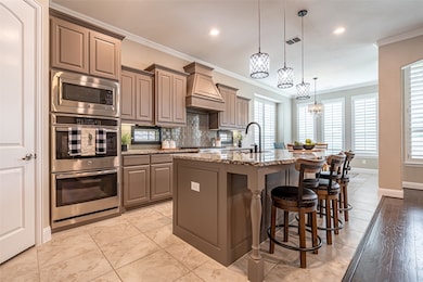 Kitchen with pendant lighting, a kitchen breakfast bar, light stone countertops, stainless steel appliances, and an island with sink