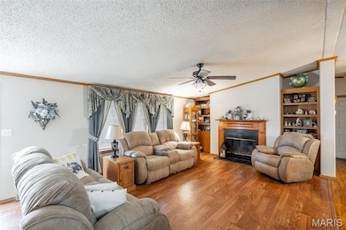 Living room with ornamental molding, a glass covered fireplace, a textured ceiling, wood finished floors, and a ceiling fan