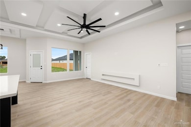 Unfurnished living room with a tray ceiling, ceiling fan, and light hardwood / wood-style flooring
