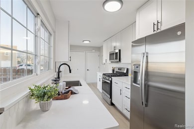 Kitchen with appliances with stainless steel finishes, white cabinetry, light wood-style floors, and light stone countertops