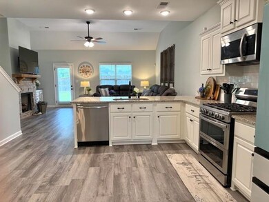 Kitchen featuring appliances with stainless steel finishes, open floor plan, a peninsula, a ceiling fan, and a fireplace