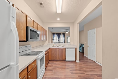 Kitchen featuring white appliances, light wood-style flooring, a textured ceiling, brown cabinets, and ceiling fan