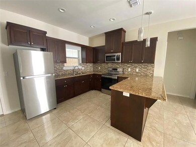 Kitchen with light tile flooring, stainless steel appliances, a kitchen breakfast bar, hanging light fixtures, and backsplash