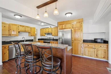 Kitchen with wood finish floors, appliances with stainless steel finishes, a kitchen breakfast bar, a kitchen island, and decorative light fixtures
