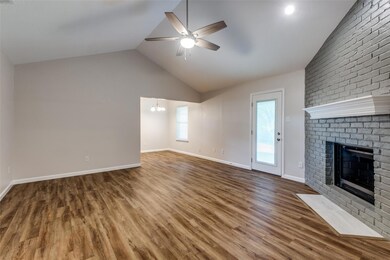 Unfurnished living room with hardwood / wood-style flooring, a fireplace, ceiling fan with notable chandelier, brick wall, and lofted ceiling