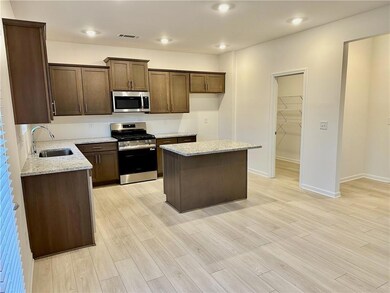 Kitchen with appliances with stainless steel finishes, light stone counters, a center island, light wood-style floors, and dark brown cabinets