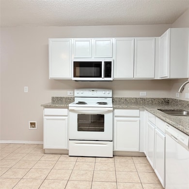 Kitchen featuring white cabinets, white appliances, light stone countertops, and a textured ceiling