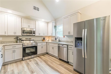 Kitchen featuring stainless steel appliances, light stone counters, light wood-style floors, and high vaulted ceiling