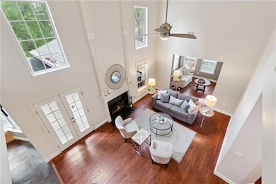 Living area with a fireplace with flush hearth, a ceiling fan, wood finished floors, a high ceiling, and baseboards