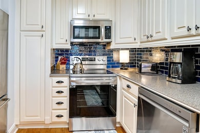 Kitchen featuring appliances with stainless steel finishes, white cabinets, tasteful backsplash, and dark countertops