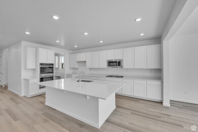 Kitchen featuring a kitchen island with sink, appliances with stainless steel finishes, white cabinets, light countertops, and recessed lighting