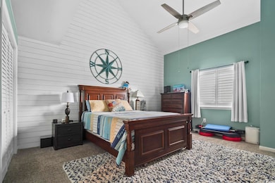 Carpeted bedroom with high vaulted ceiling, wooden walls, and a ceiling fan