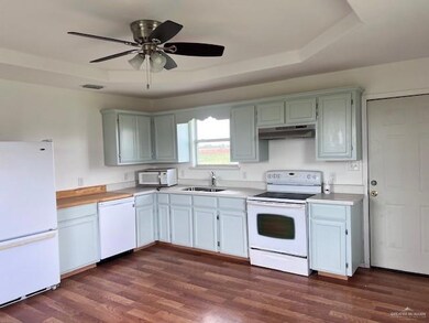 Kitchen featuring white appliances, under cabinet range hood, light countertops, a ceiling fan, and dark wood-style floors