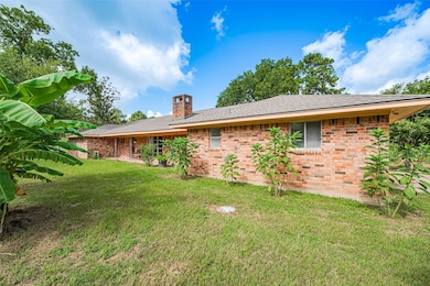 This is a charming brick ranch-style home with a spacious, well-maintained lawn. Lush greenery and mature trees surround the property, creating a serene, private atmosphere. The house features a chimney and large windows, adding to its cozy appeal.