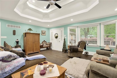 Living room with a tray ceiling, ceiling fan, recessed lighting, dark wood-style floors, and crown molding