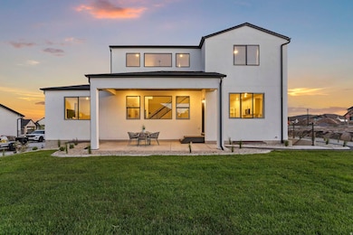 Back of property at dusk with a patio, a lawn, and stucco siding