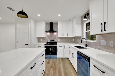 Kitchen featuring wall chimney exhaust hood, stainless steel range with electric cooktop, dishwashing machine, a sink, and light wood finished floors