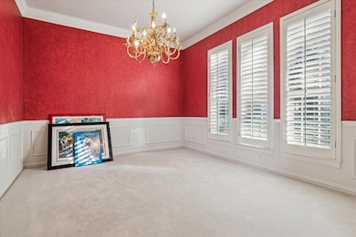 Unfurnished dining area with light carpet, a chandelier, crown molding, a decorative wall, and wainscoting