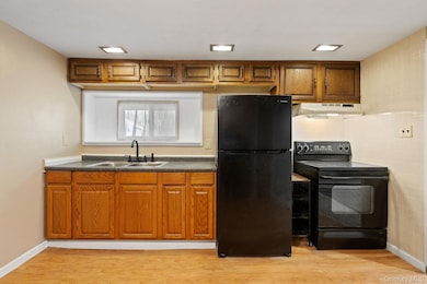 Kitchen with black appliances, brown cabinetry, dark countertops, and light wood-type flooring