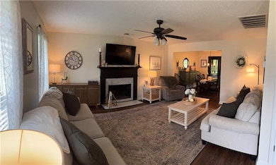 Living room featuring wood finished floors, a fireplace with flush hearth, a ceiling fan, and a textured ceiling