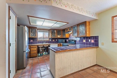 Kitchen featuring a peninsula, brown cabinets, tasteful backsplash, black appliances, and glass insert cabinets