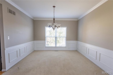 Carpeted spare room with a chandelier, crown molding, a wainscoted wall, and a decorative wall