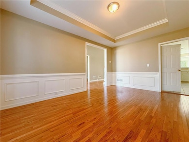 Spare room featuring a raised ceiling, crown molding, light wood-style floors, a decorative wall, and wainscoting