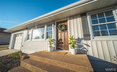 Doorway to property with board and batten siding, a garage, and driveway