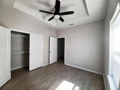Unfurnished bedroom featuring a raised ceiling, dark wood finished floors, a closet, and a ceiling fan