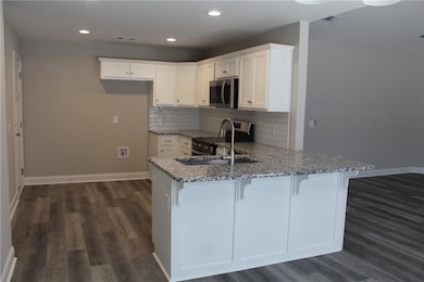 Kitchen with white cabinetry, dark wood-style floors, backsplash, light stone countertops, and recessed lighting