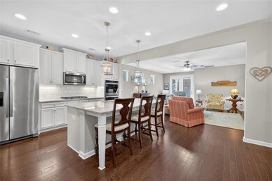 Kitchen featuring stainless steel appliances, light stone counters, white cabinets, tasteful backsplash, and a kitchen island with sink