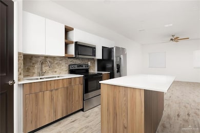 Kitchen featuring modern cabinets, light wood finished floors, a sink, open shelves, and appliances with stainless steel finishes