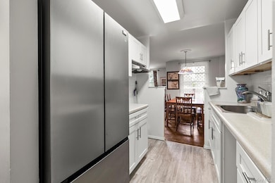 Kitchen with freestanding refrigerator, a sink, white cabinets, decorative backsplash, and light countertops