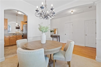 Dining room featuring arched walkways, a chandelier, ornamental molding, and light wood-style flooring